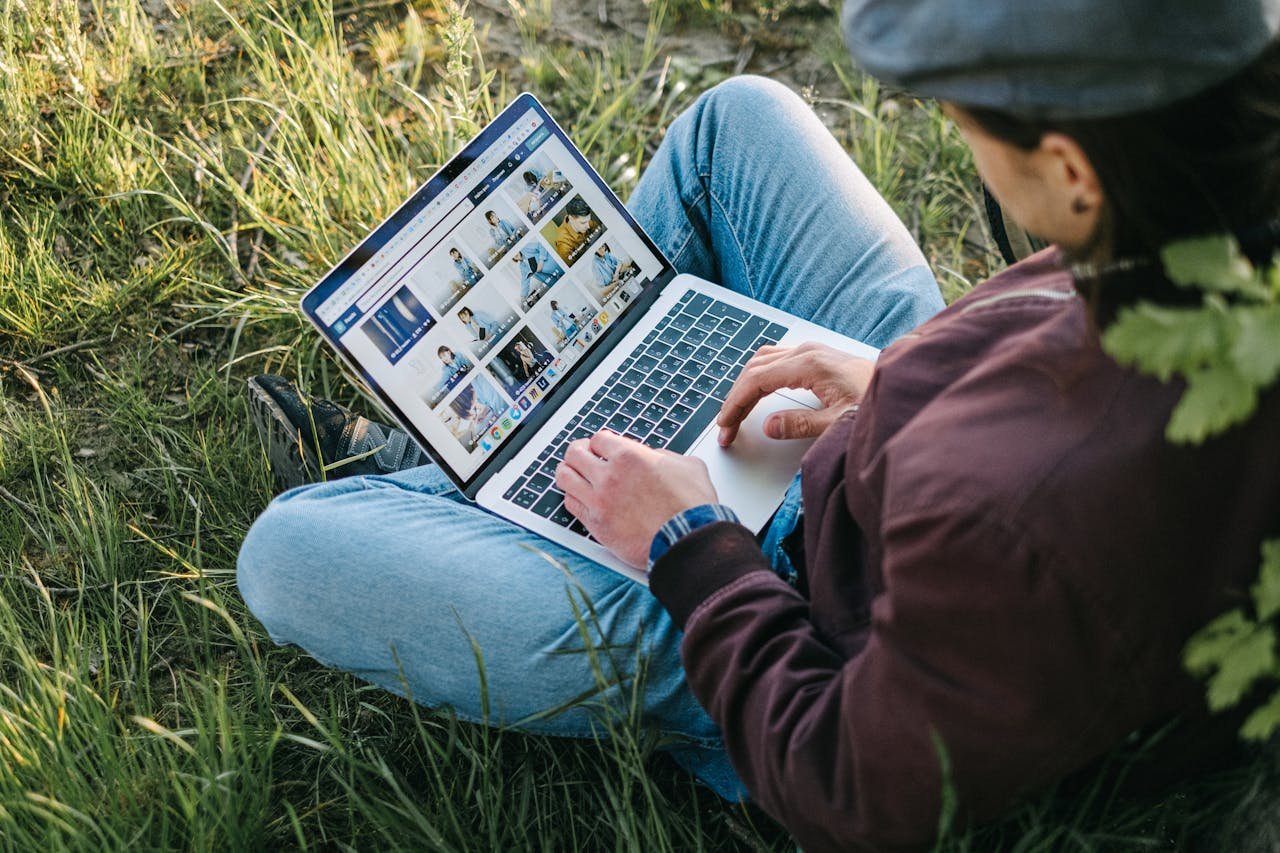 Individual typing on a laptop while sitting on grass, enjoying nature and remote work.